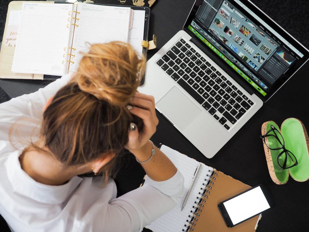 A frustrated woman with her hands on her head trying to avoid logo brand design mistaked sitting in front of a laptop computer.
